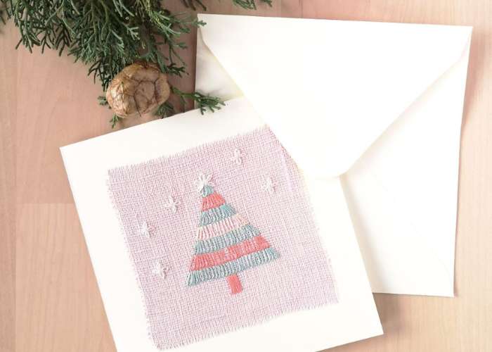 गुलाबी लिनन, सफेद लिफाफे और पाइन शंकु पर क्रिसमस ट्री कढ़ाई वाला पोस्टकार्ड