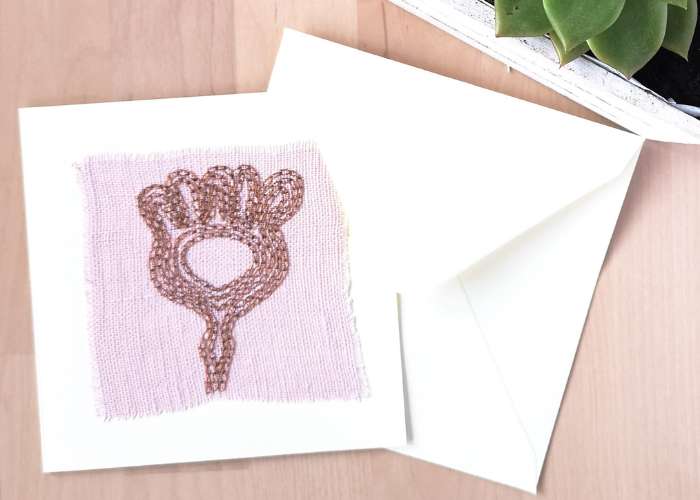 गुलाबी लिनन कपड़े पर चेन सिलाई के साथ हाथ से कढ़ाई किया गया अमूर्त पौधा कार्ड