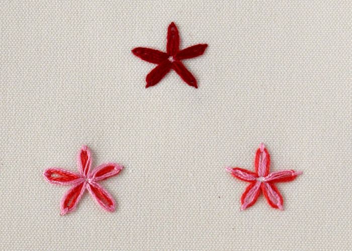 लाल और गुलाबी रंगों में आलसी डेज़ी कढ़ाई सिलाई के साथ कढ़ाई किए गए तीन फूल