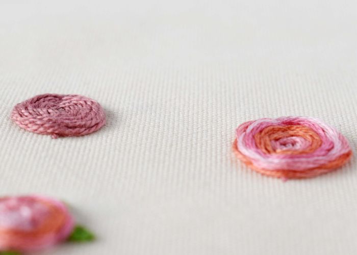 सफेद कपड़े पर बुने हुए पहिये की सिलाई से हाथ से कढ़ाई किए गए गुलाबी फूल